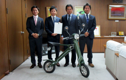 写真：折りたたみ型電動バイクを受け取る市長