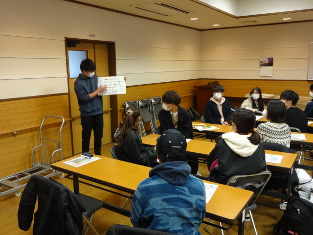 グループの代表者がホワイトボードを手に持ち話し合ったことを説明している